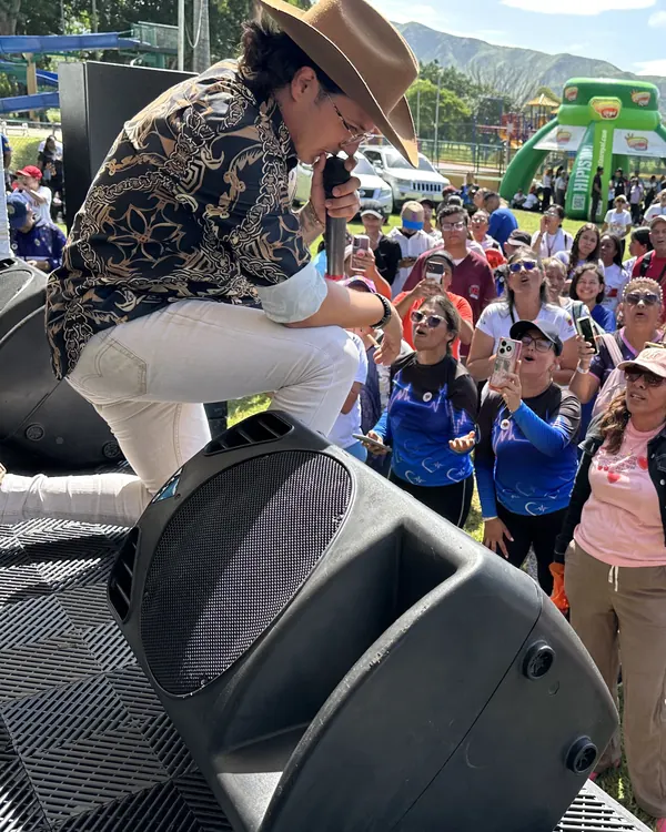 Ricardo cantando en una tarima al aire libre frente a un público numeroso