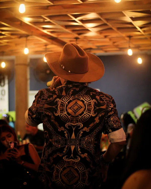 Ricardo de espaldas, con sombrero, cantando bajo luces cálidas